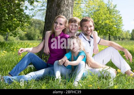 Famiglia felice di genitori e due bambini seduti sull'erba nel parco primaverile Foto Stock