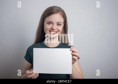 Sorridente giovane donna caucasica ragazza tenendo bianco foglio di carta con spazio per le copie Foto Stock