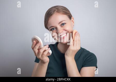 Sorridente giovane donna caucasica ragazza sta mettendo il suo fondamento della polvere di make up Foto Stock