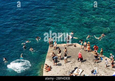 Gruppo di persone che nuotano e si abbronzano nel mare del piccolo villaggio di Vernazza, cinque Terre, patrimonio dell'umanità dell'UNESCO. La Spezia, Liguria, Italia Foto Stock