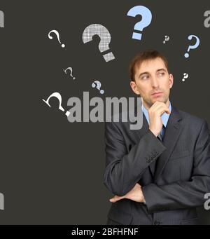 Uomo che pensa circondato da domanda su sfondo scuro Foto Stock