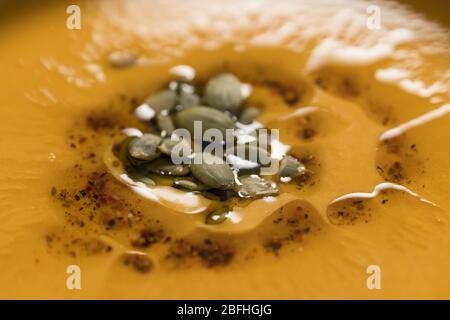 Zuppa di zucca decorata con olio di semi di zucca in ciotola bianca su fondo concreto primo piano Foto Stock