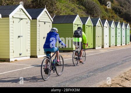 Bournemouth, Dorset Regno Unito. 19 aprile 2020. Tempo nel Regno Unito: Bella calda giornata di sole come le temperature aumentano alle spiagge di Bournemouth sulla costa meridionale come la gente prende il loro esercizio consentito, la maggior parte aderendo alle linee guida di Coronavirus. I ciclisti percorrono la passeggiata passando davanti alle capanne sulla spiaggia mantenendo la loro distanza - equitazione biciclette. Credit: Carolyn Jenkins/Alamy Live News Foto Stock