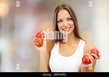 Bella giovane donna con pomodori su sfondo luminoso Foto Stock