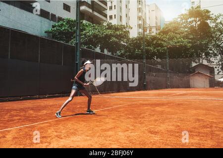Una giovane donna afro-americana sottile gioca a tennis all'aperto nel campo di allenamento; bella ragazza biraciale sport in posizione sportiva pronta a deviare dieci