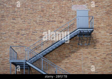 Scala esterna in acciaio che conduce ad una porta chiusa su un muro di mattoni rossi. Concetto per l'edilizia e l'industria, struttura e architettura, cli Foto Stock