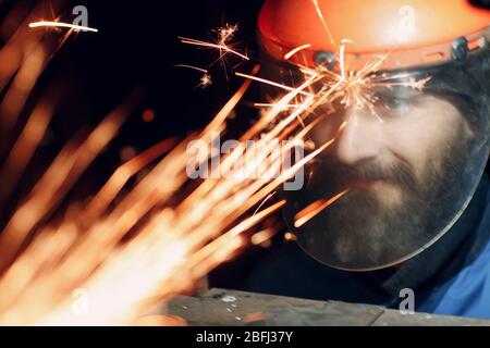 Uomo in maschera protettiva trasparente lavora su metallo con sega circolare. Scintille e faccia. Foto Stock