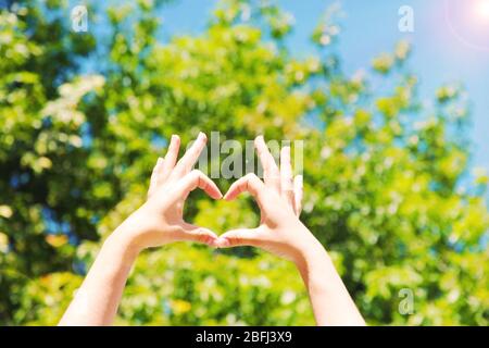 Le mani della giovane donna che fanno la cornice di forma del cuore sullo sfondo della natura Foto Stock