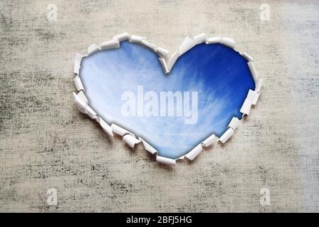 Sfondo blu cielo con nuvole attraverso il foro a forma di cuore in carta Foto Stock