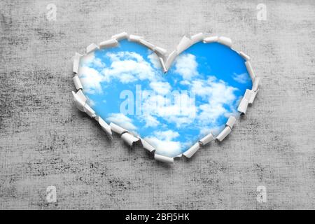 Sfondo blu cielo con nuvole attraverso il foro a forma di cuore in carta Foto Stock