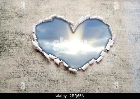 Sfondo blu cielo con nuvole attraverso il foro a forma di cuore in carta Foto Stock