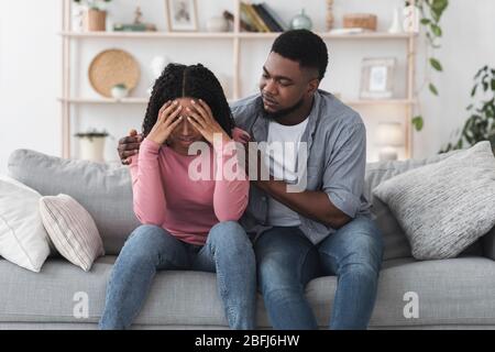 Fidanzato nero attento confortando la sua ragazza sconvolgente piangendo a casa Foto Stock