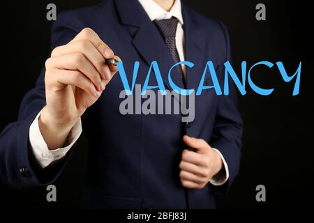 Uomo d'affari che scrive VACANCY alla lavagna trasparente, primo piano Foto Stock