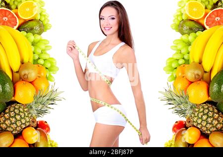 Bella giovane donna che misura il suo corpo con nastro isolato su bianco in cornice di frutta tropicale Foto Stock