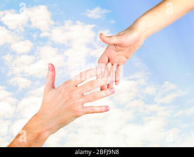 La mano della donna va alla mano dell'uomo su sfondo cielo soleggiato Foto Stock