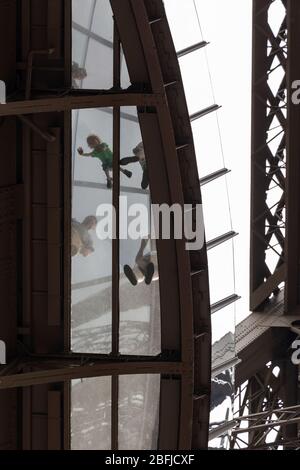 Un bambino che striscia sulla piattaforma trasparente al primo piano della Torre Eiffel come visto dal basso, Parigi Foto Stock
