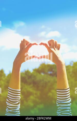 Le mani della giovane donna che fanno la cornice di forma del cuore su sfondo blu del cielo Foto Stock