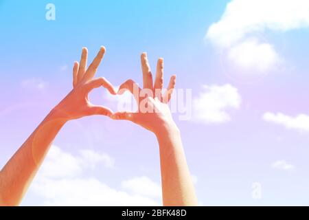 Le mani della giovane donna che fanno la cornice di forma del cuore su sfondo blu del cielo Foto Stock