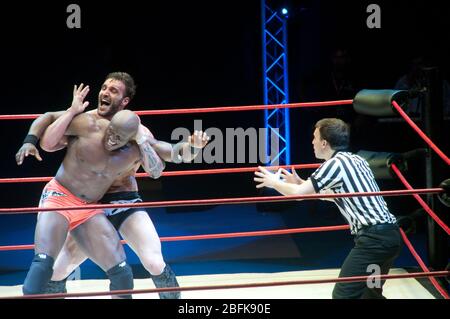 Due lottatori professionisti maschili che lottano sul ring accanto a un arbitro, in una partita di wrestling all'aperto nella città di Doha, in Qatar. Foto Stock
