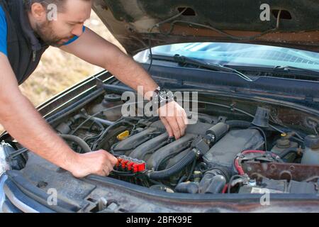 L'uomo guarda attentamente il motore sotto il cofano durante un guasto e controlla la bobina di accensione. Foto ravvicinata. Foto Stock