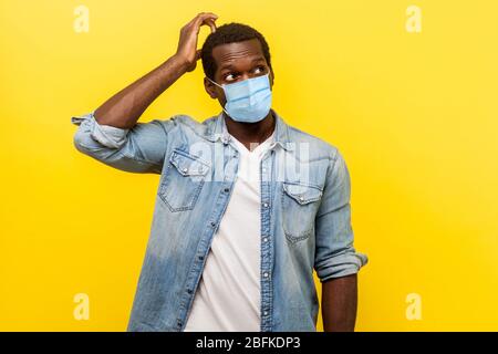 Dubbio, necessità di pensare. Ritratto di giovane incerto con maschera medica chirurgica guardando in alto, graffiando la testa mentre pensa con il viso confuso e confuso Foto Stock