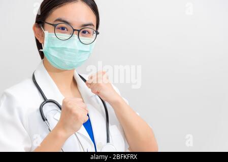 Bella giovane donna asiatica medico in uniforme bianca e maschera proteggere Coronavirus, medico sollevare i pugni per sostenere il paziente nella lotta contro le malattie Foto Stock