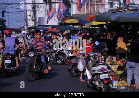 Cambogiani, alcuni sulle motociclette, indossando maschere di protezione viso / rivestimenti, andare a fare shopping al di fuori del mercato russo durante la pandemia coronavirus. Phnom Penh, Cambogia. © Kraig Lieb Foto Stock