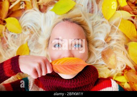 giovane ragazza che giace tra foglie autunnali, nascondendo labbra dietro una foglia Foto Stock