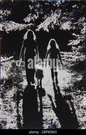 Fine anni '70 nero e bianco nero nero fotografia ritratto estremo di due bambini e il loro cane a piedi nel bosco Foto Stock