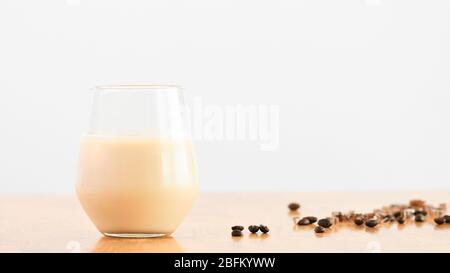 Un bicchiere di latte di soia su fondo bianco e rovere con chicchi di caffè. Concetto per la bevanda e la bevanda biologica a base di piante, dieta vegana e vegetariana, lui Foto Stock