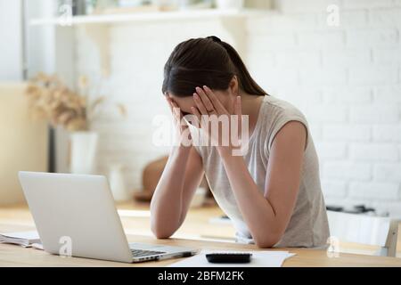 Sconvolgere la donna che tocca la testa utilizzando la calcolatrice e il laptop per il calcolo. Foto Stock