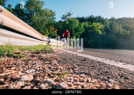 Montare maschio ciclista biker in sella alla sua moto ciclo su una strada asfaltata al tramonto mentre il sole tramonta attraverso la sua ruota. Foto Stock