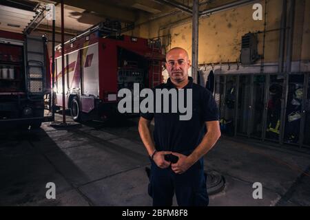 Ritratto di bel pompiere in piedi contro camion presso la stazione di fuoco Foto Stock