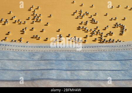 Vista ravvicinata della maschera medica blu e piccoli pezzi di perle d'argento su sfondo giallo. Foto concettuale come protezione da diversi tipi di Foto Stock