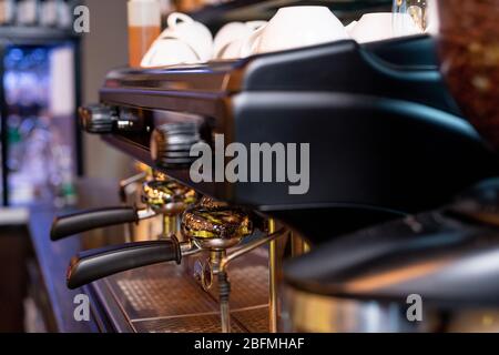 Moderna macchina da caffè con due manici in plastica nera, interruttori sopra di essi e mucchio di tazze in porcellana bianca per cappuccino Foto Stock