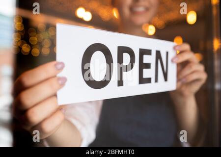Mani di un giovane cameriere o proprietario di un ristorante o di un caffè che mette l'avviso aperto sulla porta all'inizio della giornata lavorativa Foto Stock