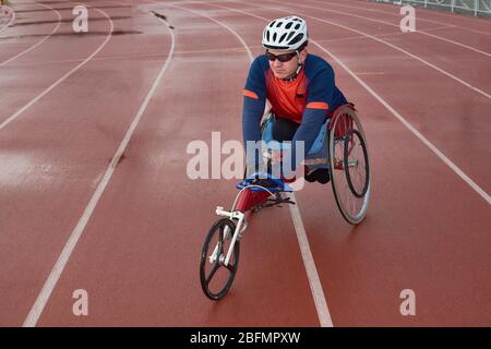 Futuro campione Paralimpico. Paraplegico atleta maschile seduto su sedia a rotelle specializzata e si riscalda in pista prima della gara Foto Stock