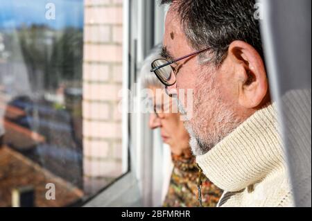 Concetto di quarantena di coronavirus e di allontanamento sociale. Coppia senior, a casa guardando attraverso la finestra con espressione preoccupata. Rimani a casa. Anziani e pensionati . Foto Stock