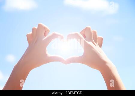 Mani femminili a forma di cuore su sfondo blu cielo Foto Stock