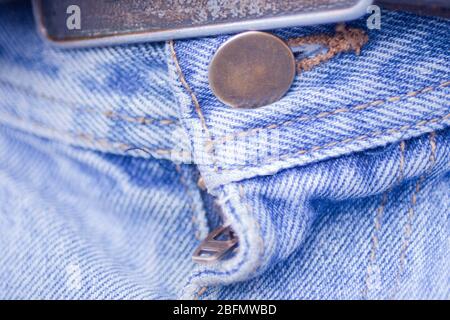 Chiudi una fibbia, un bottone e una zip di jeans blu. Visualizzazione macro di bottoni, zip e texture di tessuto denim blu sbiadito. Foto Stock