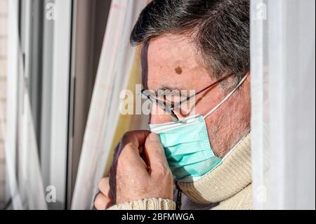 uomo anziano con maschera protettiva per il viso, a casa guardando attraverso la finestra. Concetto di quarantena di coronavirus rimanere a casa e distanza sociale. Lockdown persone. Anziani e vita in pensione . Foto Stock