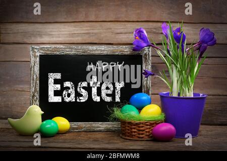 Biglietto di auguri di Pasqua. Uova colorate con fiori e lavagna su sfondo di legno Foto Stock