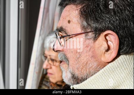 Concetto di quarantena di coronavirus e di allontanamento sociale. Coppia senior, a casa guardando attraverso la finestra con espressione preoccupata. Rimani a casa. Anziani e pensionati . Foto Stock