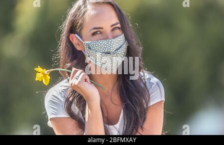 La ragazza bruna in natura indossa la maschera sorridente, tenendo un daffodil in mano. Foto Stock