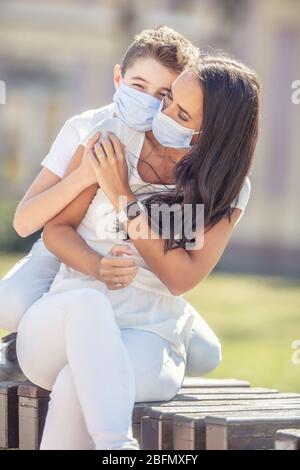 Ragazzo abbracciando la madre dalla schiena, tenendosi le mani all'aperto, con maschere facciali. Foto Stock