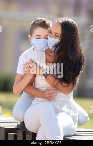 Ritratto di un ragazzo che abbrancava la madre dalla schiena, tenendo le mani all'aperto, con maschere facciali. Foto Stock