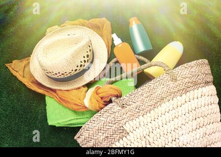 Borsa in vimini con sciarpa, cappello e bottiglie di lozioni su sfondo verde alla luce del sole. Stile retrò Foto Stock