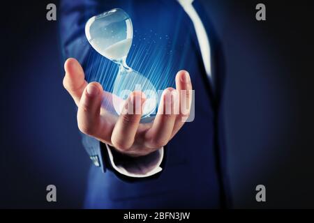 Uomo d'affari che tiene la clessidra in mano su sfondo scuro Foto Stock