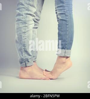 Giovane donna in piedi sul ragazzo piedi su sfondo grigio Foto Stock