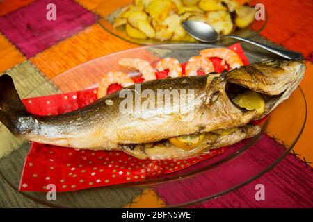 vista su un branzino cotto in casa su un vassoio di vetro e un piatto con patate al forno Foto Stock